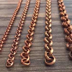 May include: Five vertical copper chains of varying thicknesses arranged side by side. Each chain consists of interlocking round metal links, displaying a metallic reddish-brown color and a consistent circular pattern throughout their length.