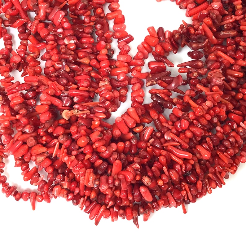 May include: A strand of bright red coral beads, perfect for jewelry making. The beads are various shapes and sizes, with some being long and thin, while others are shorter and rounder.
