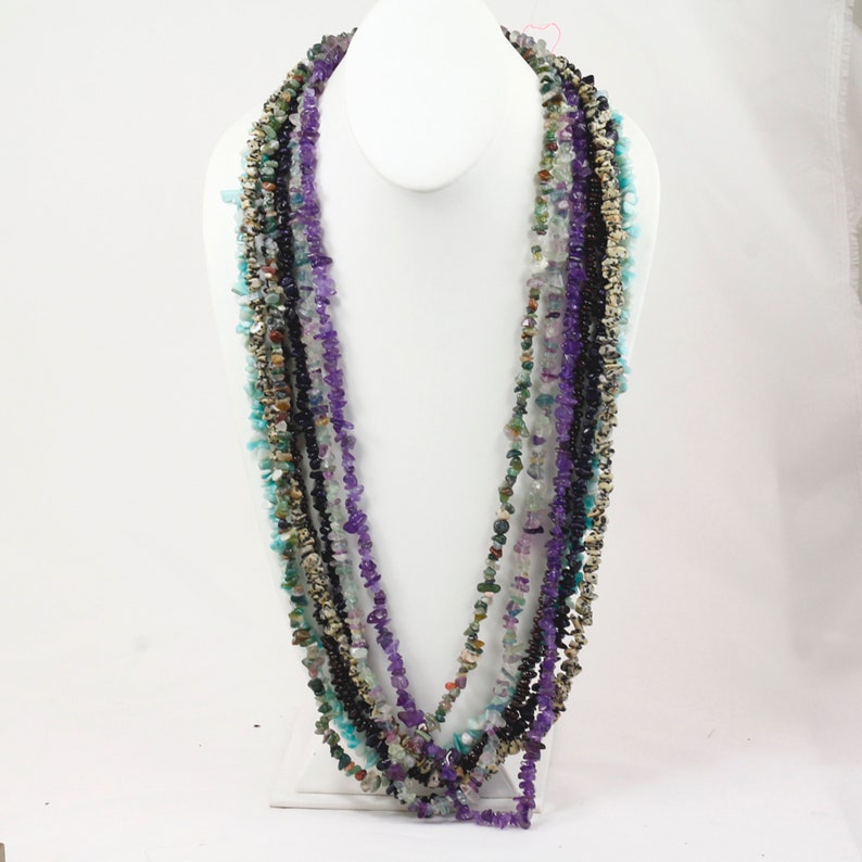May include: Multi-strand necklace made of various semi-precious stones, including amethyst, turquoise, and black onyx. The necklace is layered and features a variety of shapes and sizes of stones.