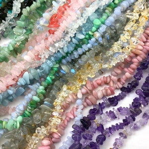 May include: Assortment of chip-shaped gemstone beads in various colors, including green, blue, pink, yellow, and purple. The beads are arranged in rows, showcasing the different colors and textures.