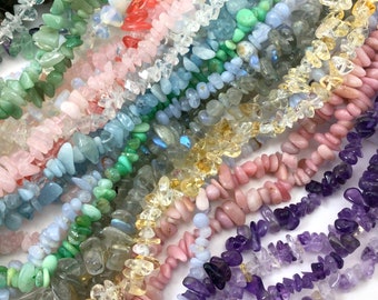 May include: Assortment of chip-shaped gemstone beads in various colors, including green, blue, pink, yellow, and purple. The beads are arranged in rows, showcasing the different colors and textures.