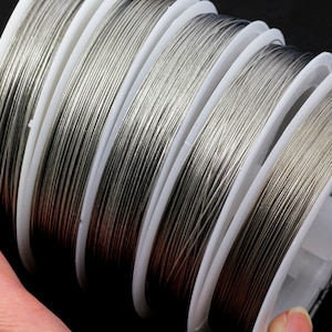 May include: Close-up of spools of silver-colored wire. The wire is wound around white plastic spools.