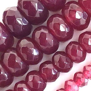May include: A strand of deep red faceted gemstone beads. The beads are round and have a smooth, polished finish.