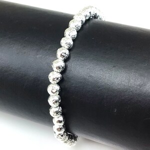 May include: A silver beaded bracelet with a textured surface. The bracelet is made of round, irregularly shaped beads strung together. The beads have a metallic sheen and are displayed against a black background.