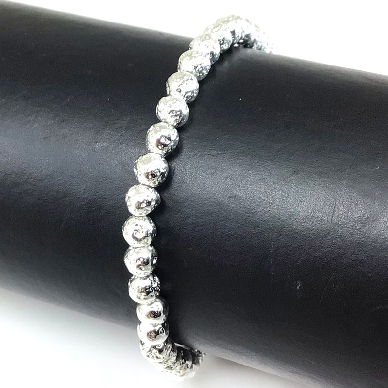 May include: A silver beaded bracelet with a textured surface. The bracelet is made of round, irregularly shaped beads strung together. The beads have a metallic sheen and are displayed against a black background.