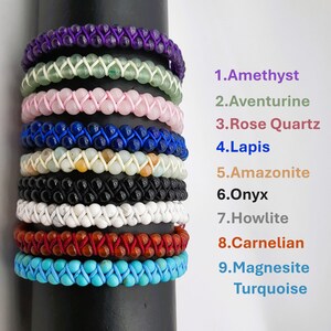 May include: A stack of nine bracelets made of different gemstones, including amethyst, aventurine, rose quartz, lapis lazuli, amazonite, onyx, howlite, carnelian, and magnesite turquoise. Each bracelet is a different color and has a unique pattern.