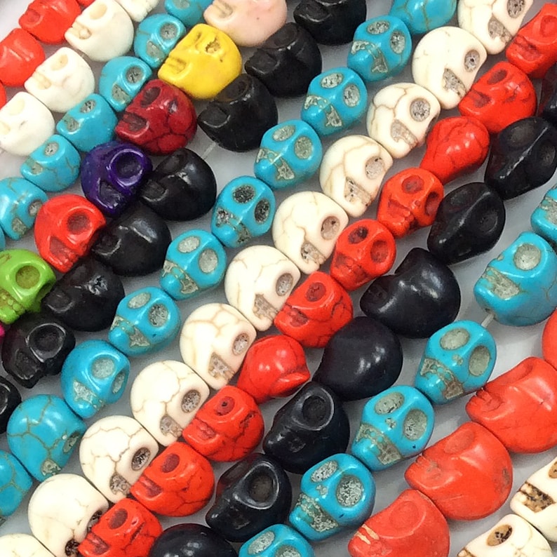 Puede incluir: Una colecci&oacute;n de cuentas de calavera de colores hechas de varios materiales, incluyendo turquesa, rojo, blanco, negro y verde. Las cuentas tienen todas la forma de una calavera y tienen una variedad de dise&ntilde;os diferentes.
