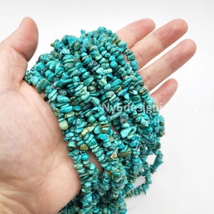 May include: A handful of turquoise chip beads, showcasing a vibrant mix of blue and green hues. The irregular shapes and sizes of the stones create a textured appearance. The beads are strung together, suggesting their use in jewelry making or crafting.