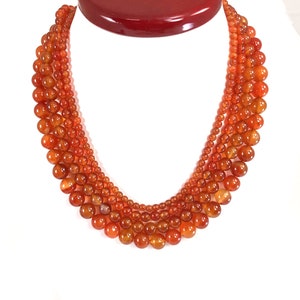 Pu&ograve; includere: Una collana multifilo realizzata con perline di cornalina. Le perline sono rotonde e di colore arancione. La collana &egrave; a strati e ha una dimensione delle perline graduata.