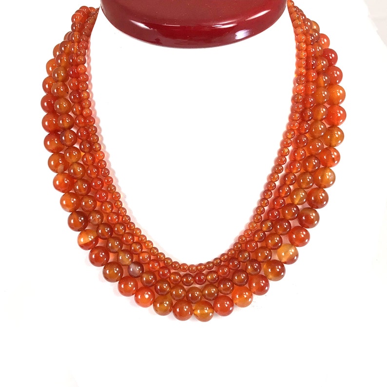 Pu&ograve; includere: Una collana multifilo realizzata con perline di cornalina. Le perline sono rotonde e di colore arancione. La collana &egrave; a strati e ha una dimensione delle perline graduata.