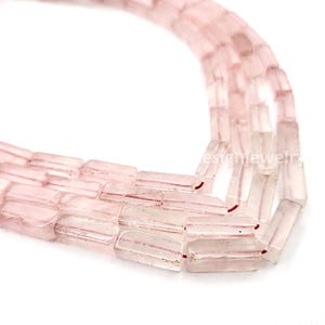 May include: Close-up of strands of rectangular, translucent pink beads. Each bead has a subtle pink stripe. The beads are strung together, creating a delicate and elegant appearance. The background is white.
