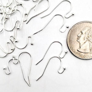 May include: A collection of silver-colored earring hooks with a small ball at the end of each hook. A U.S. quarter is included for size reference. The hooks are arranged on a white surface.