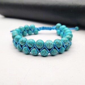 May include: A turquoise blue beaded bracelet with a knotted cord. The beads are round and have a slightly rough texture.