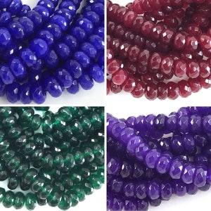 May include: Assortment of faceted gemstone beads in four colors: blue, red, green, and purple. The beads are all the same size and shape, and they are arranged in rows.