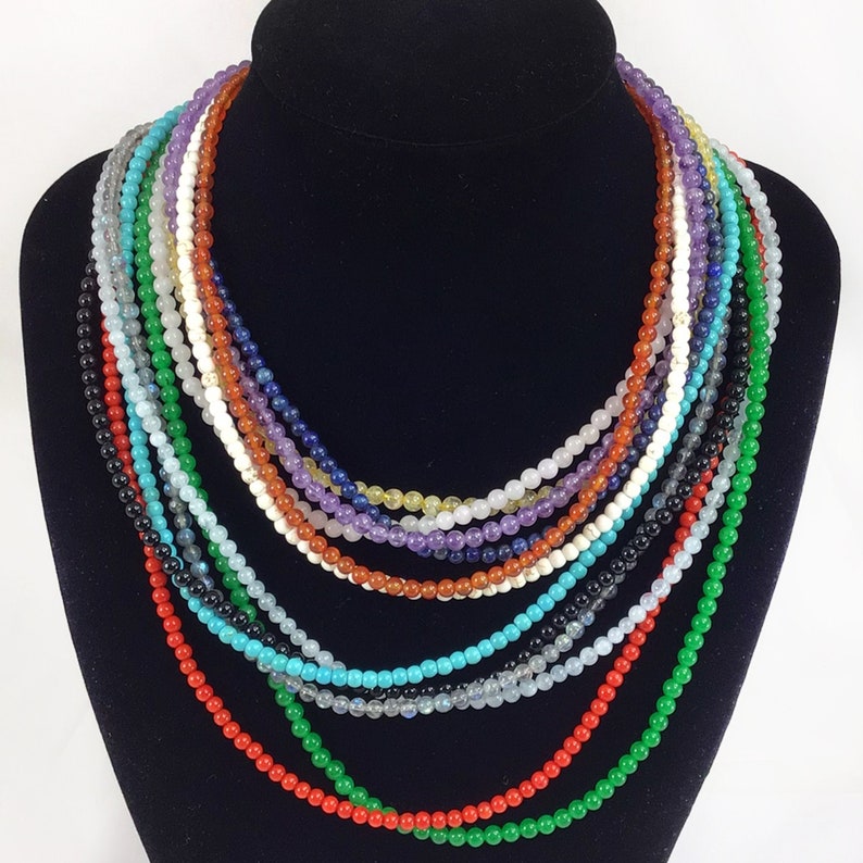 May include: A multi-strand necklace made of various gemstone beads, including turquoise, amethyst, and carnelian. The necklace is displayed on a black mannequin bust.