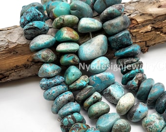 May include: Strands of turquoise gemstone beads in various shades of blue, green, and brown. The beads are irregularly shaped and appear to be polished. The beads are strung together, ready for jewelry making. The background includes a piece of wood.