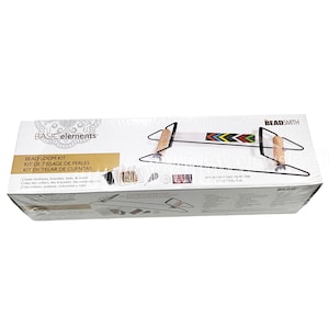 May include: A Basic Elements bead loom kit. The box features the text "BEAD LOOM KIT" and "Create necklaces, bracelets, belts, & more!" The loom itself is black with wooden handles and a beaded design in the center.