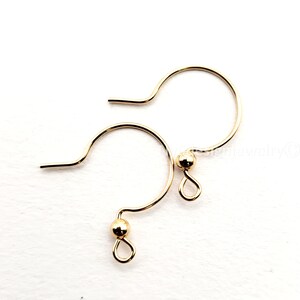 May include: Two gold-colored earring hooks. Each hook has a curved design with a small ball and a loop at the bottom. The hooks are designed for jewelry making and are set against a white background.