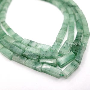 May include: Close-up of strands of green aventurine gemstone beads. The beads are rectangular, with a polished finish and visible inclusions. The beads are strung together on a green string, perfect for jewelry making.