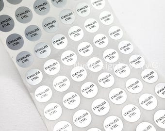 May include: A sheet of small, circular stickers. Each sticker is silver with the words "STAINLESS STEEL" printed in black. The stickers are arranged in rows and columns, with some stickers appearing in a lighter shade of silver.