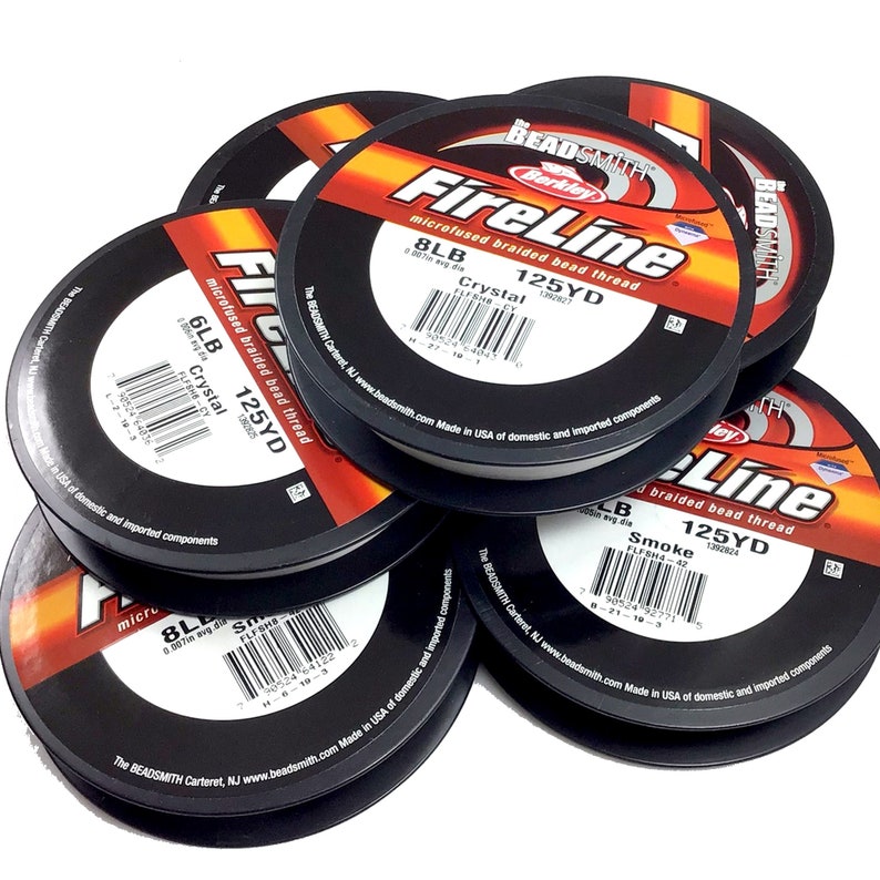 May include: A close-up of six spools of white FireLine microfused braided bead thread. The spools are labeled with the brand name, product name, and size. The spools are stacked on top of each other.
