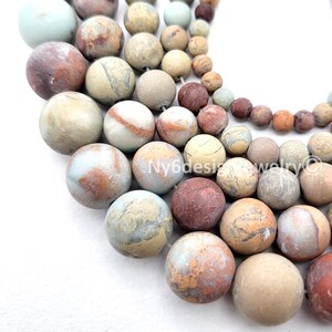 May include: Assorted natural stone beads in various sizes and colors, including brown, beige, and blue-gray. The beads have a matte finish and are strung together, perfect for jewelry making. The image shows a close-up of the beads.