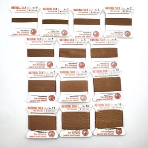 May include: A collection of brown natural silk thread spools, labeled with sizes from 0.30 mm to 1.05 mm. Each spool is on a white card with text indicating it's for stringing pearls and beads. The text "NATURAL SILK" is printed on each card.