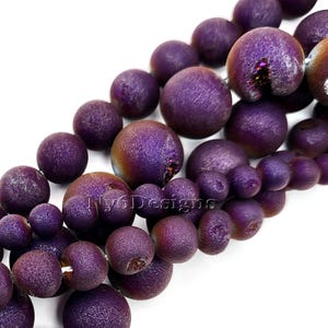 May include: Close-up of a strand of purple beads with a textured surface. The beads vary in size and have a metallic sheen, with hints of gold and iridescent colors. The beads are strung together, ready for jewelry making.