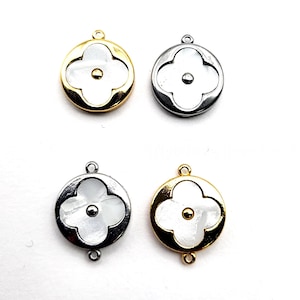 May include: Four round charms with a clover design. Two charms have a gold-colored border, and two have a silver-colored border. Each charm features a white clover design with a small, round accent in the center. The charms have small loops for attaching to jewelry.