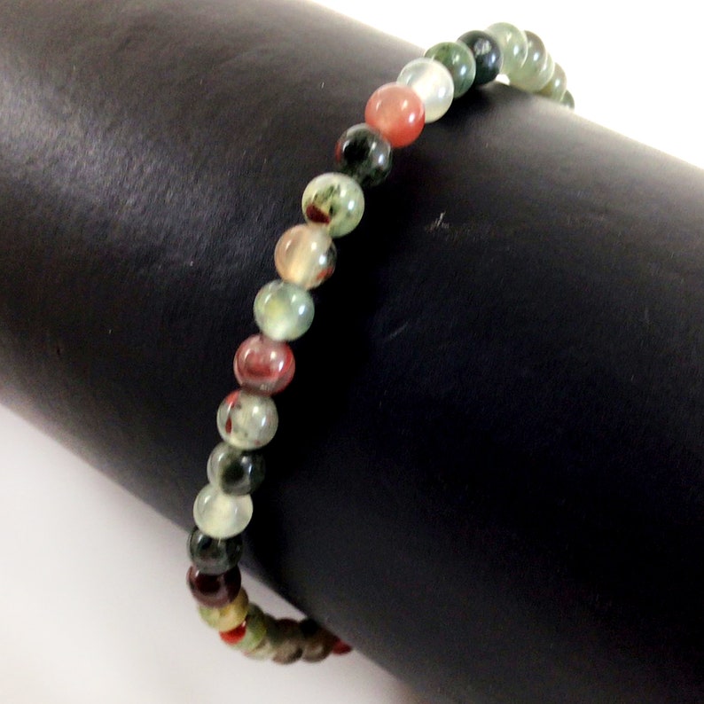 May include: A multi-colored beaded bracelet with green, red, and white beads. The bracelet is made of natural stone and is approximately 7 inches in length.