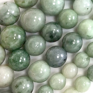 May include: A collection of smooth, round, green jade beads. The beads are various shades of green, from light to dark.