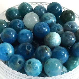 May include: A collection of blue agate beads with a hole drilled through the center of each bead. The beads are round and have a smooth, polished finish.
