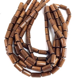 May include: Strands of dark brown wooden beads. Each bead is cylindrical with rounded edges. The beads are strung together, creating a necklace or craft supply. The wood grain is visible, adding texture and warmth to the design.