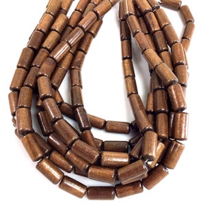 May include: Strands of dark brown wooden beads. Each bead is cylindrical with rounded edges. The beads are strung together, creating a flowing, organic shape. The beads have a polished finish, reflecting light. Ideal for jewelry making or craft projects.