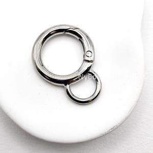 May include: A silver-colored round clasp with a small attached ring. The clasp has a hinged opening mechanism. The item is shown on a white surface.