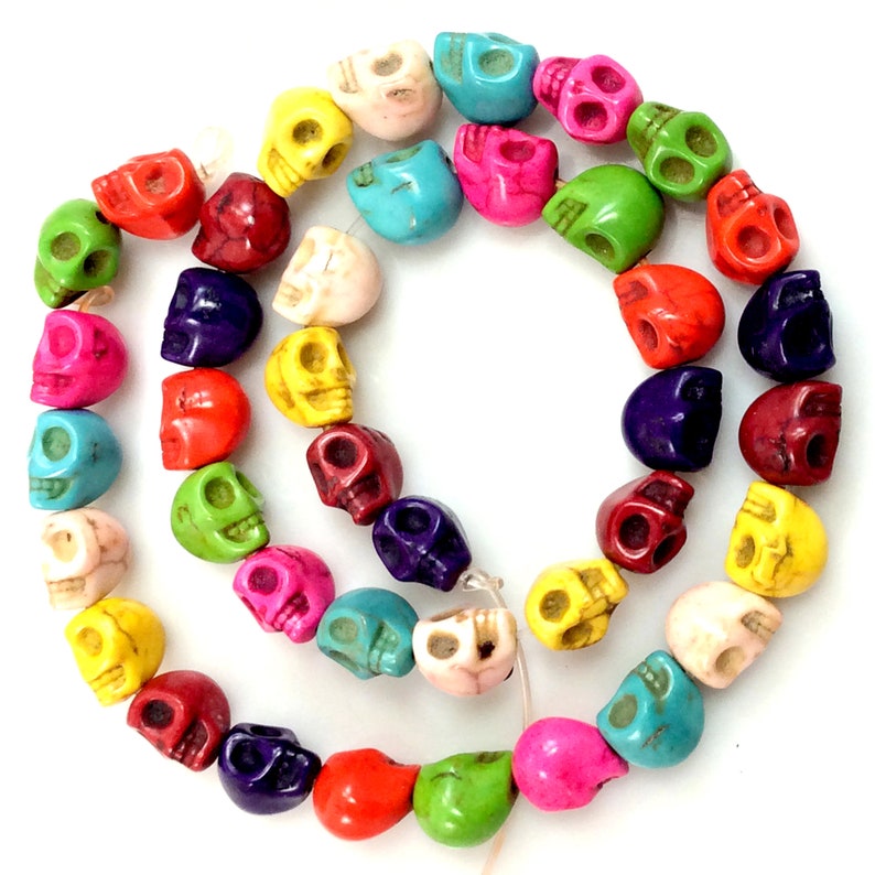 Puede incluir: Una hebra de cuentas de calavera de color turquesa. Las cuentas son de varios colores, incluyendo rojo, naranja, amarillo, verde, azul, morado y blanco.