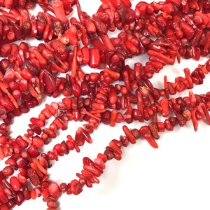 May include: A strand of red coral beads, featuring a variety of shapes and sizes. The beads are arranged in a loose pile, showcasing their natural beauty.