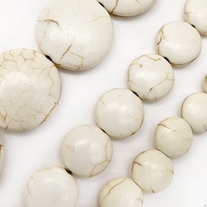 May include: A strand of white, round, smooth, and slightly textured beads. The beads are all different sizes and are strung together on a clear thread.