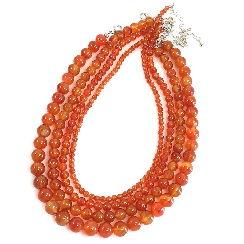 Pu&ograve; includere: Una collana multifilo realizzata con perle di cornalina di diverse dimensioni. Le perle sono di colore arancio intenso e hanno una finitura liscia e lucida.