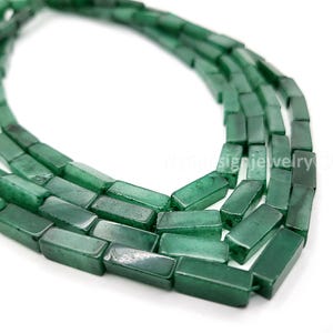 May include: Close-up of strands of green rectangular beads. The beads are a deep emerald green color and appear to be made of a polished stone. The beads are strung together, creating a necklace or bracelet.