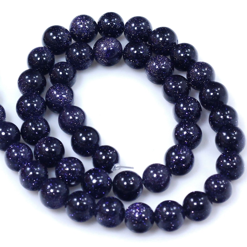 May include: A strand of dark blue gemstone beads with a speckled, starry appearance. The beads are round and smooth, and they are strung together on a clear thread.