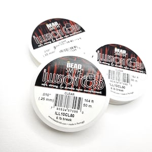 May include: Three spools of clear illusion cord for jewelry making. Each spool has a black and red label with the text "ILLUSION CORD" and "CLEAR". The cord is .010" (.25 mm) thick and 164 ft (50 m) long.