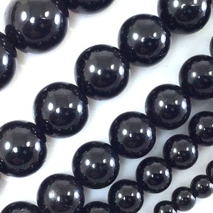 May include: A strand of black gemstone beads. The beads are round and smooth, and they have a high polish. The beads are strung on a clear elastic cord.