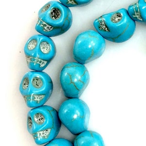 Puede incluir: Una hebra de cuentas de calavera de color azul turquesa con vetas doradas. Las cuentas son lisas y pulidas, y los detalles de la calavera est&aacute;n bien definidos.