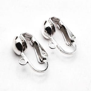 May include: A pair of silver clip-on earring backs. The backs are made of metal and have a smooth, rounded surface.
