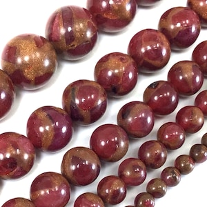May include: A strand of round, red and gold gemstone beads. The beads have a marbled, swirled pattern.