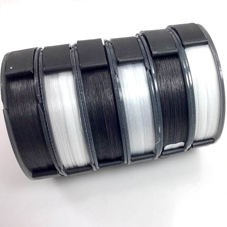 May include: Four spools of fishing line, two black and two white, are stored in a black plastic container.