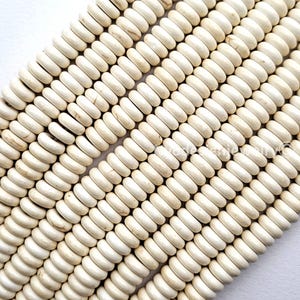 May include: Close-up of off-white, cylindrical beads arranged in diagonal rows. The beads have a slightly irregular shape and a matte finish, suggesting a natural material. The beads are strung together, ready for jewelry making or other crafts.