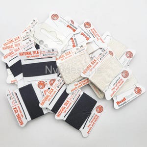 May include: Assortment of natural silk thread spools in various colors and sizes, labeled "Natural Silk" with the thread thickness in millimeters. The spools are packaged on white cards with red text that reads "For stringing pearls and beads".