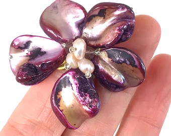 May include: A purple and gold flower-shaped ring made of iridescent shell with white pearl accents.